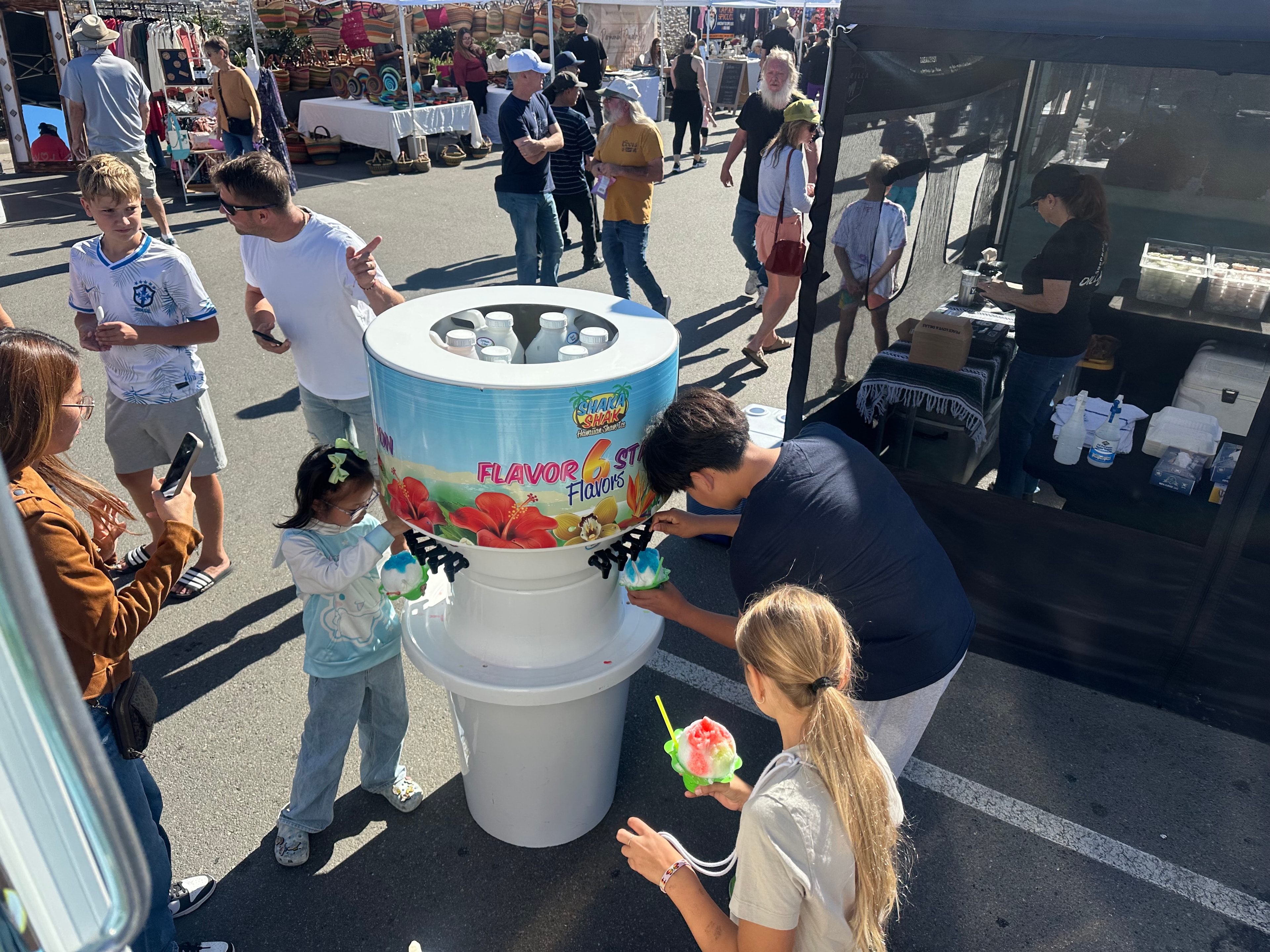 Families enjoying shave ice at the Shaka Shak flavor station at an outdoor market