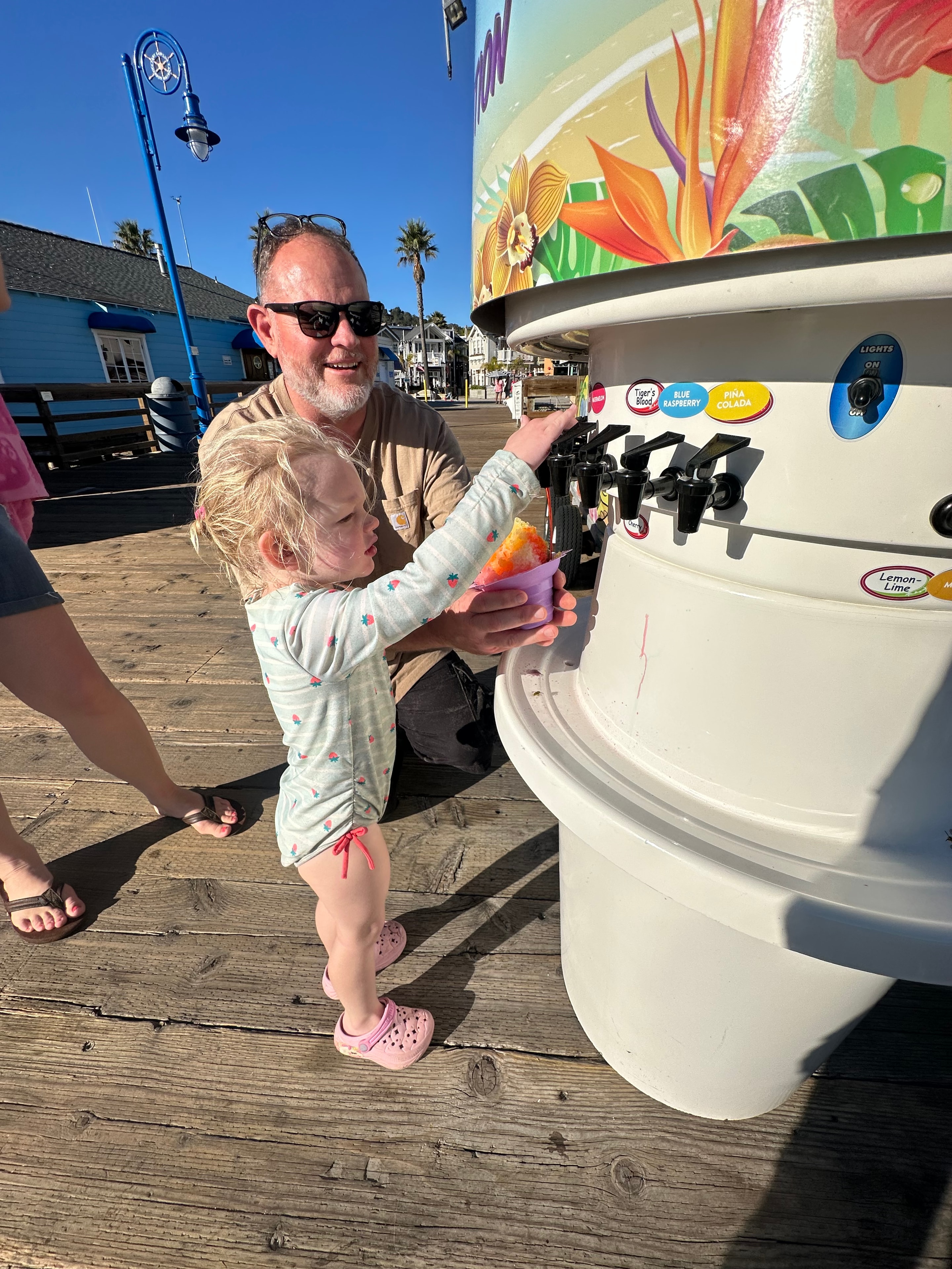 Dad holding a yellow shave ice for his daughter at the Shaka Shak pier kiosk