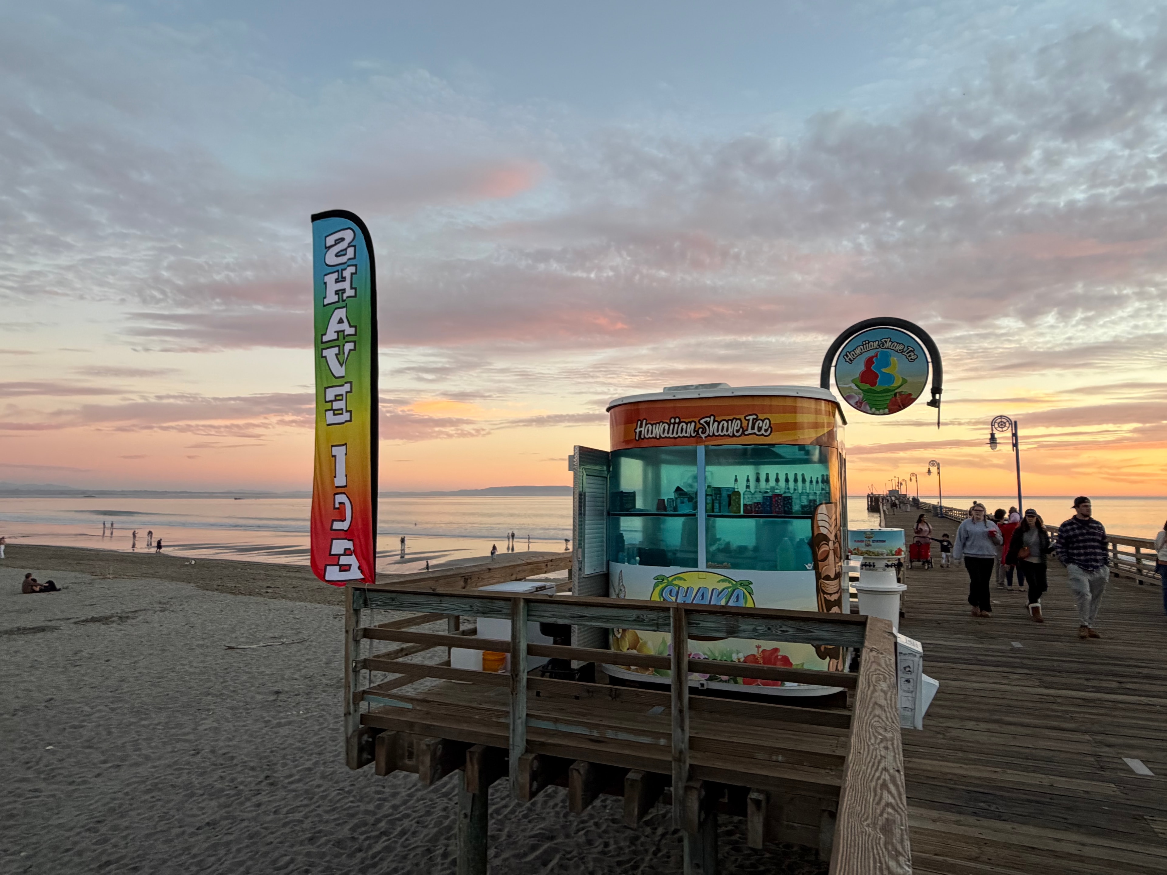 Shaka Shak Hawaiian Shave Ice kiosk on the Avila Beach pier at sunset with crowd