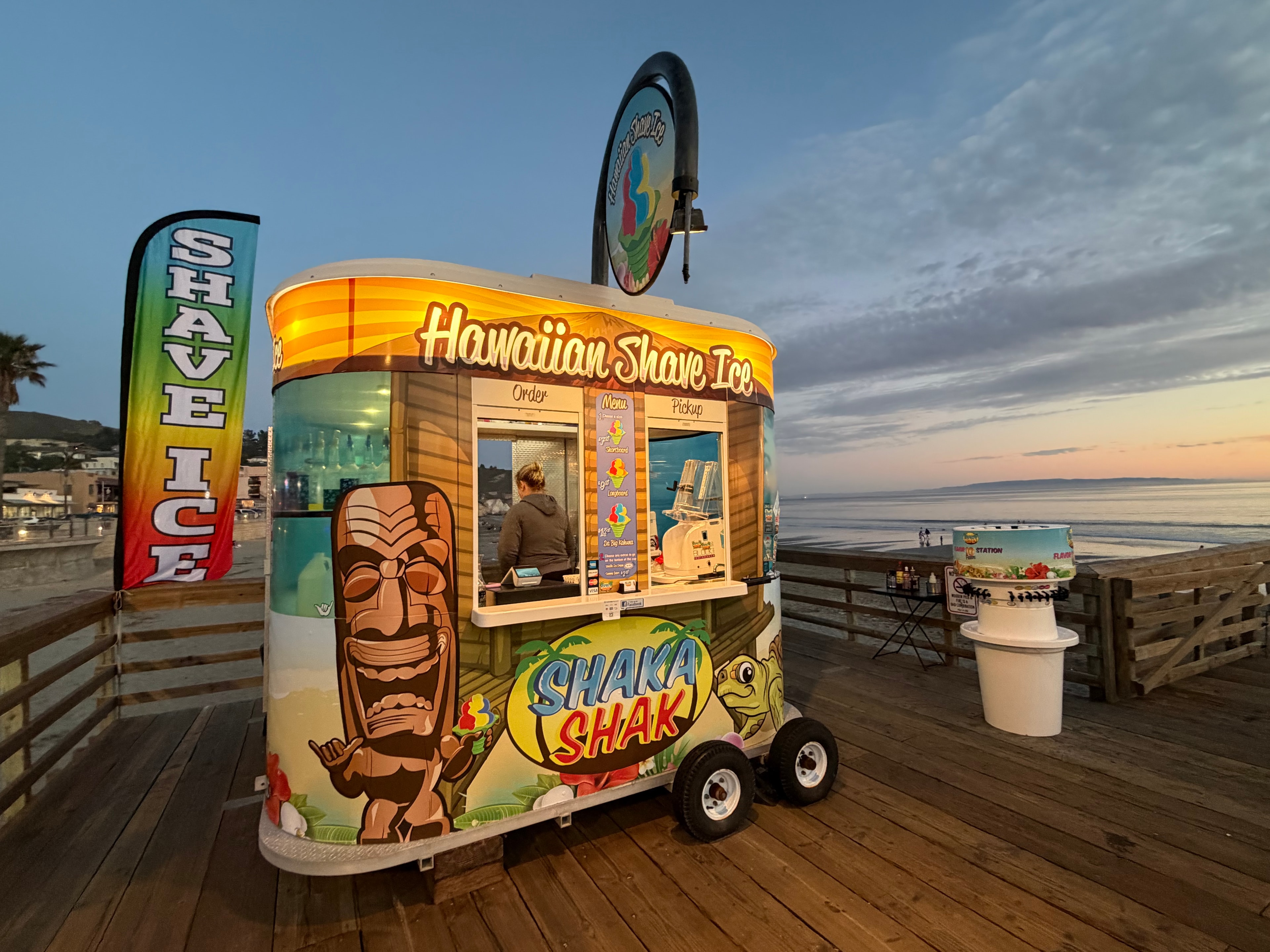 Shaka Shak kiosk glowing at dusk on the Avila Beach pier with ocean view