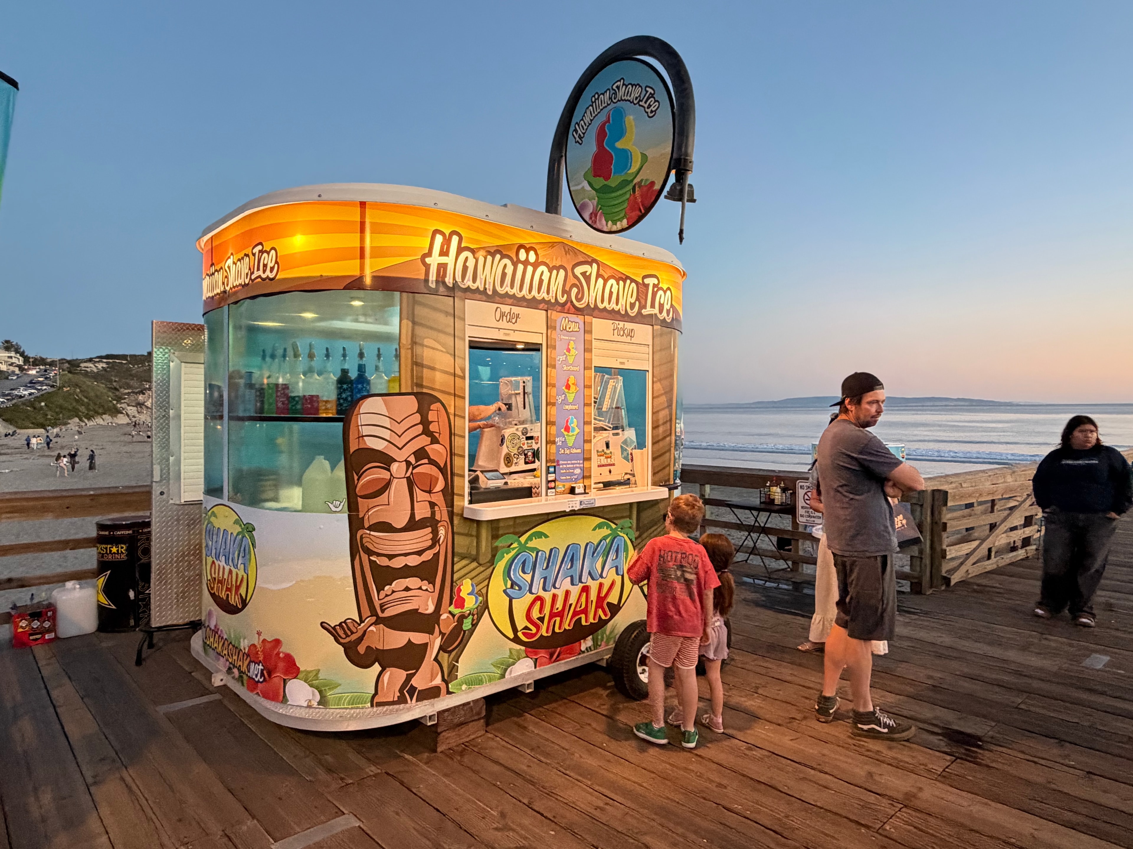 Shaka Shak Hawaiian Shave Ice kiosk on the pier at twilight with family