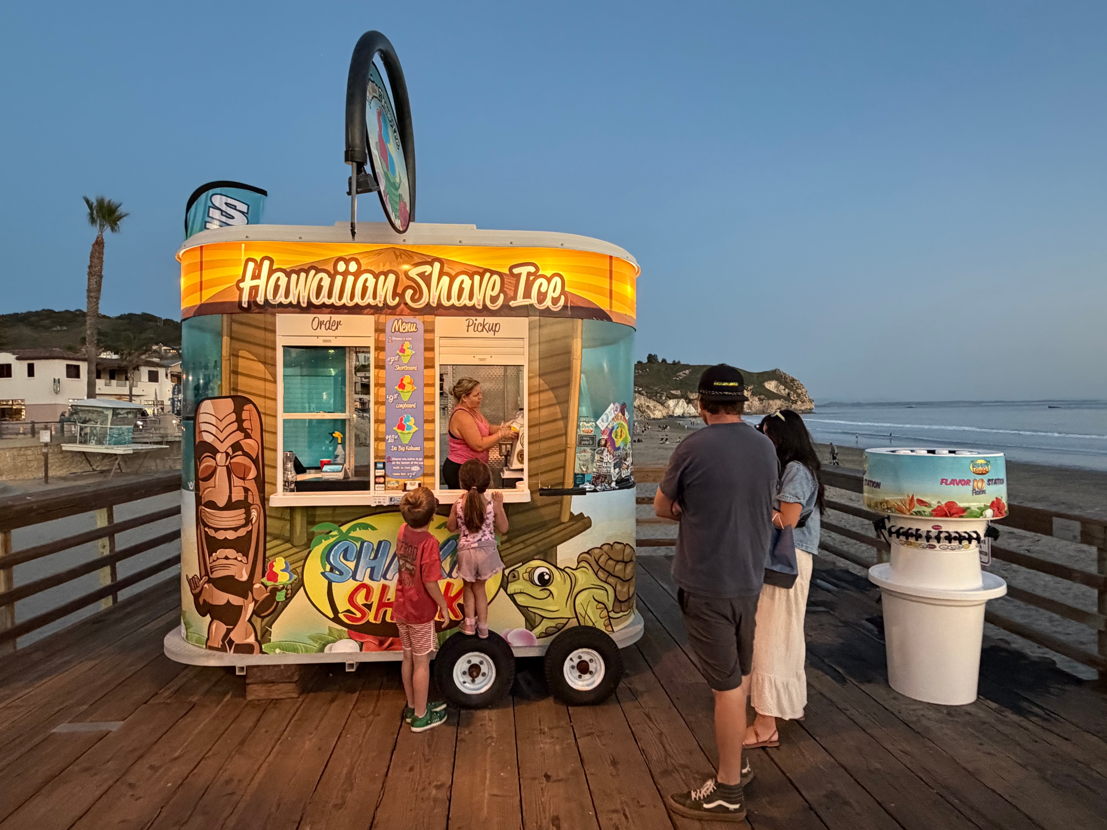 Shaka Shak kiosk on the Avila Beach pier at dusk with family ordering