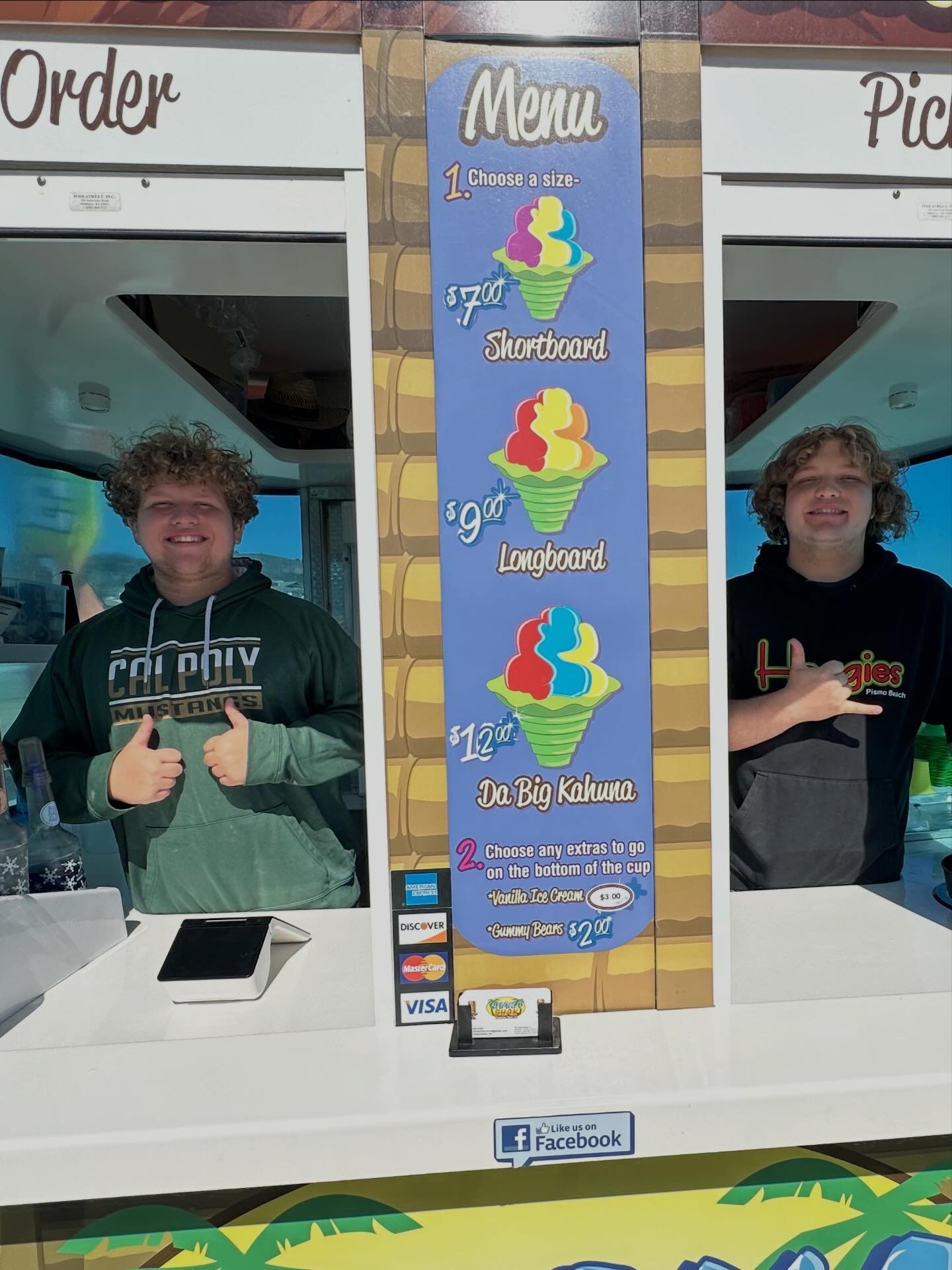 Shaka Shak staff smiling with the menu board showing Shortboard, Longboard, Da Big Kahuna