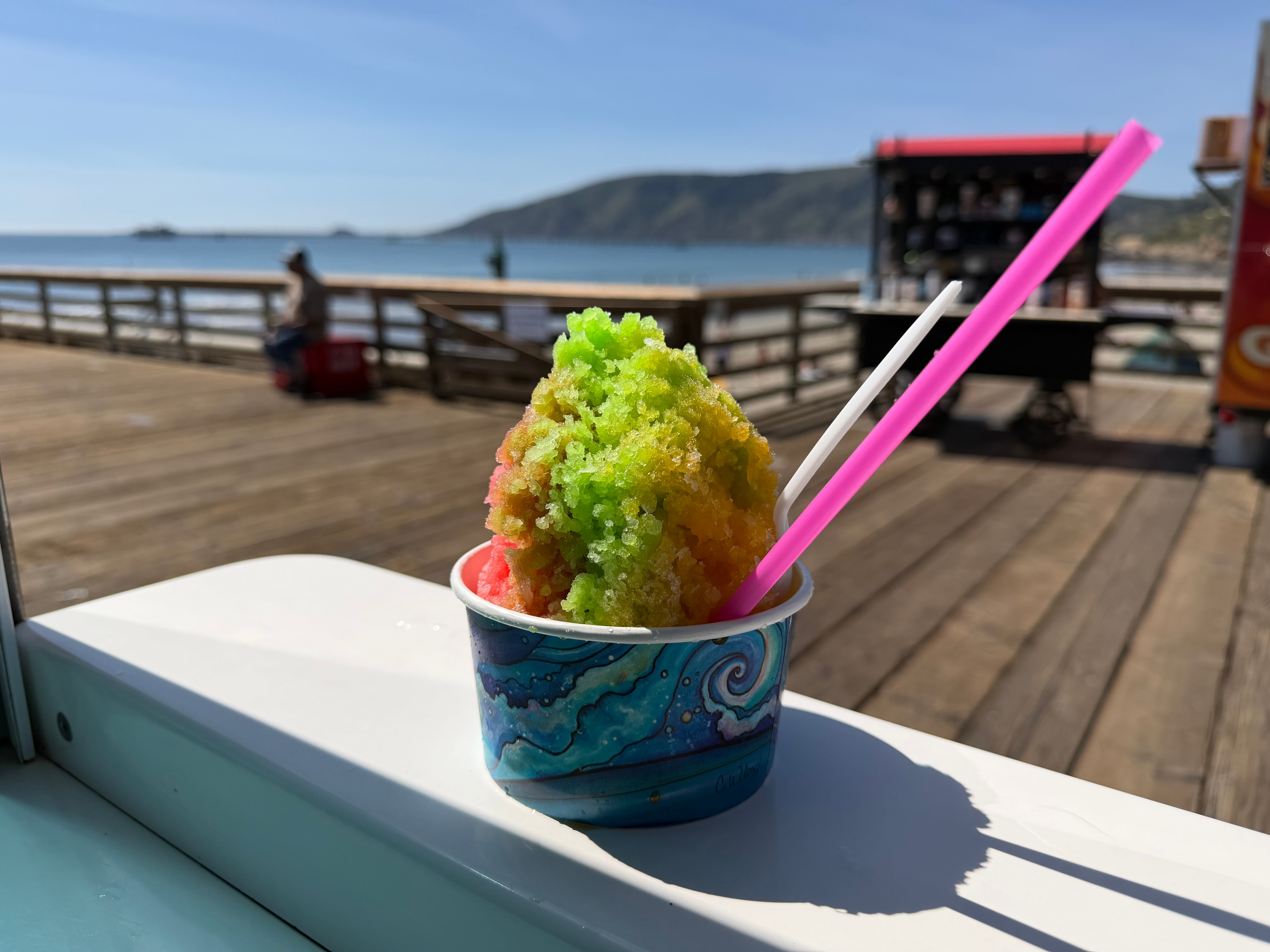 Colorful green and red shave ice in a wave-print cup on the Avila Beach pier