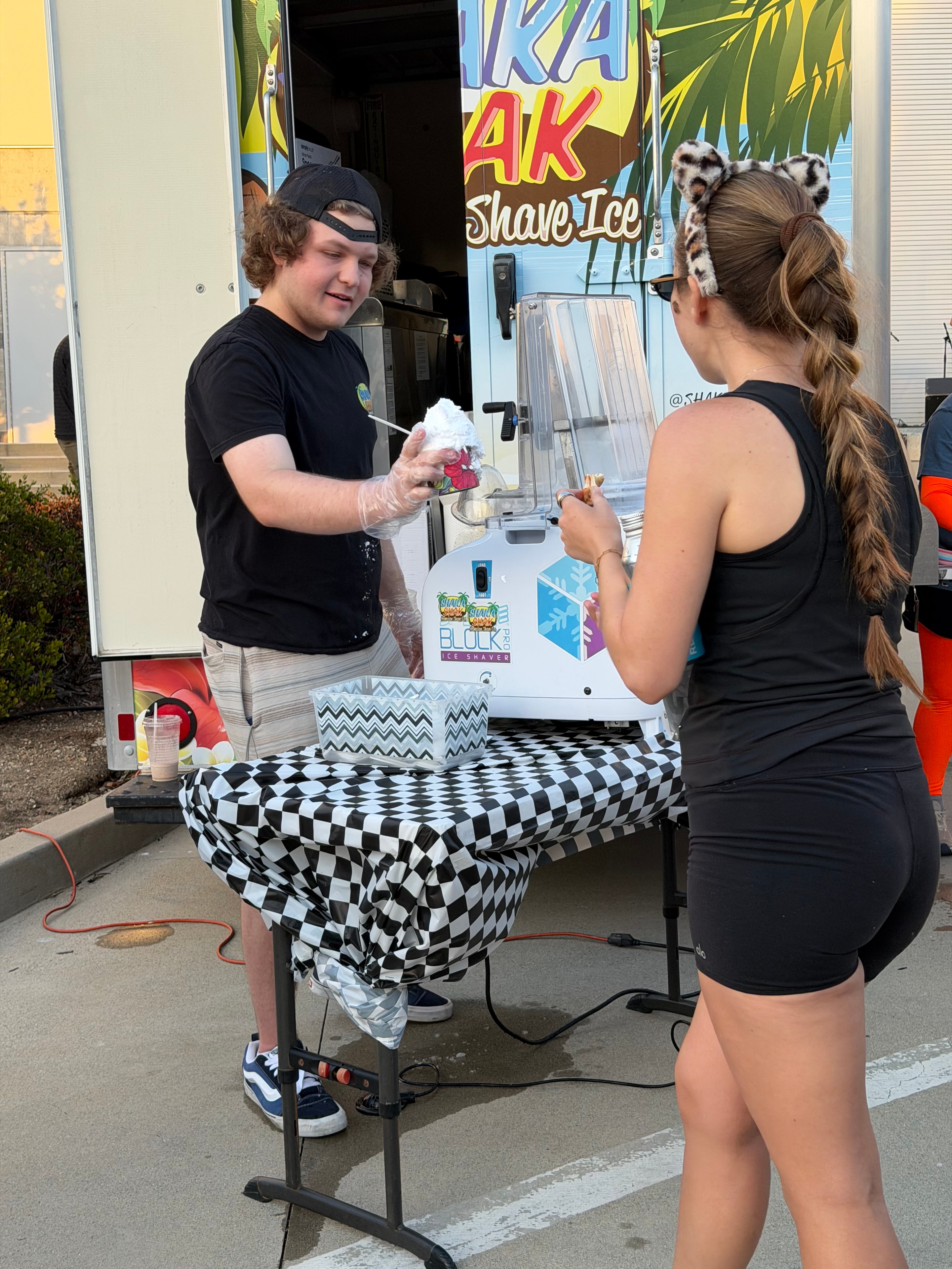 Shaka Shak staff member making shave ice at an outdoor event with a customer