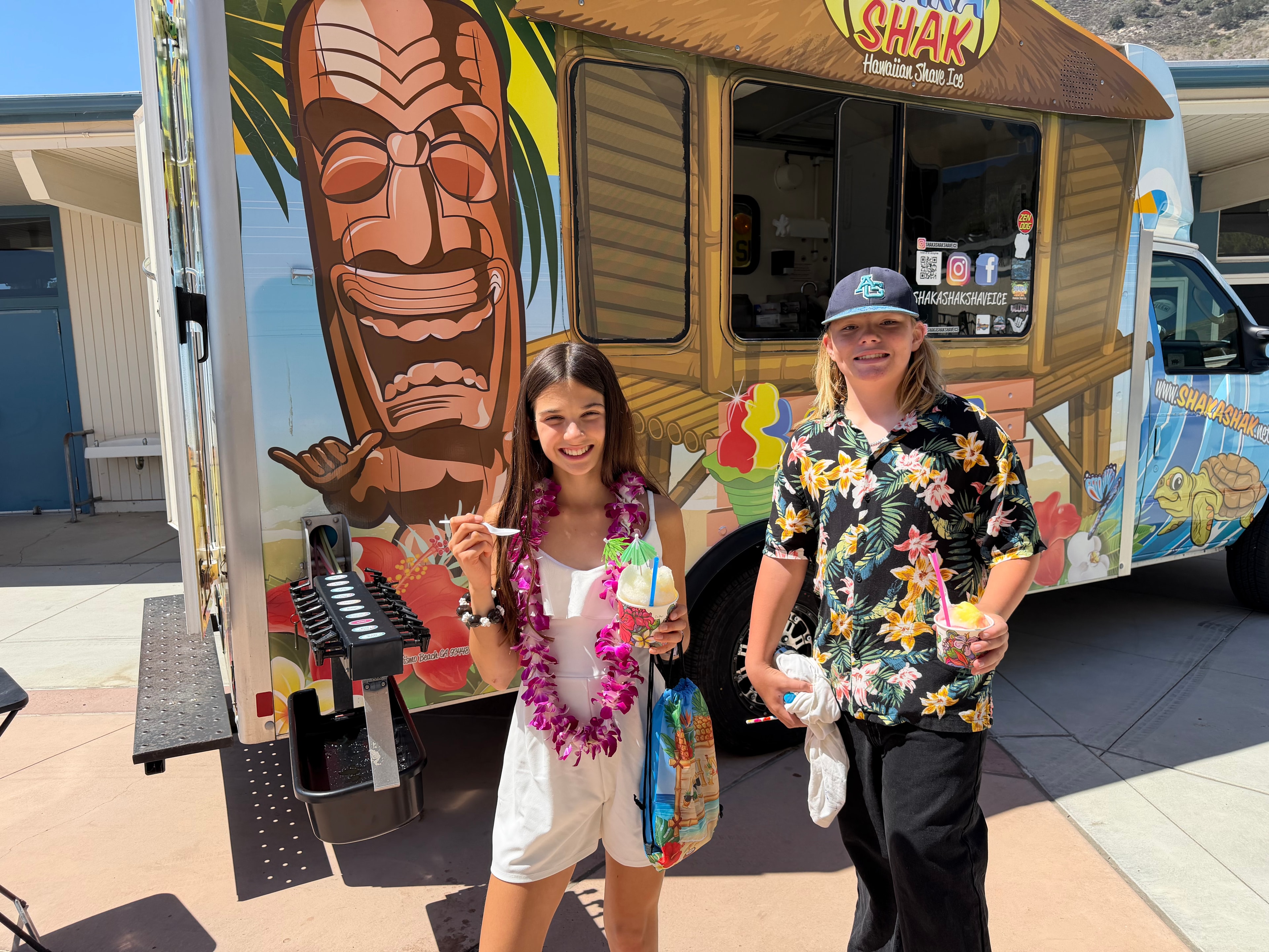 Two kids posing with shave ice in front of the Shaka Shak Hawaiian Shave Ice truck