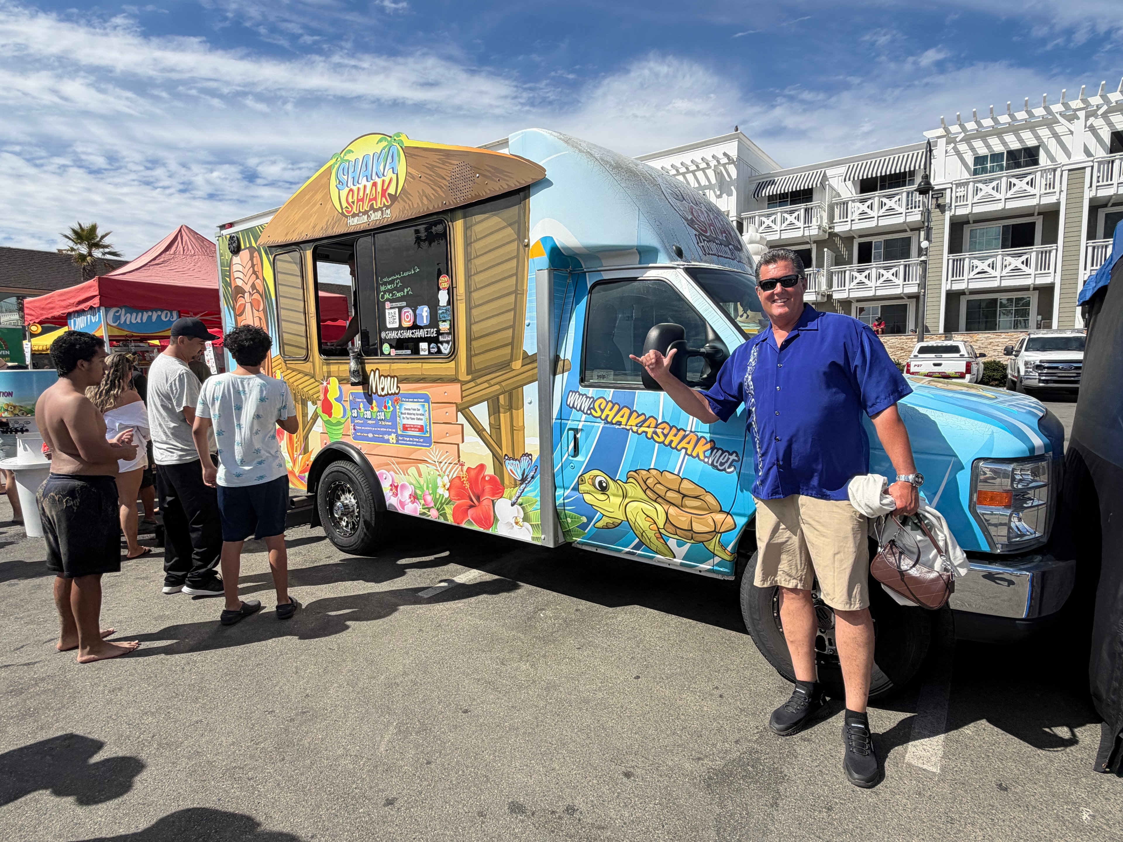 Owner giving a shaka sign in front of the Shaka Shak truck at a beach event