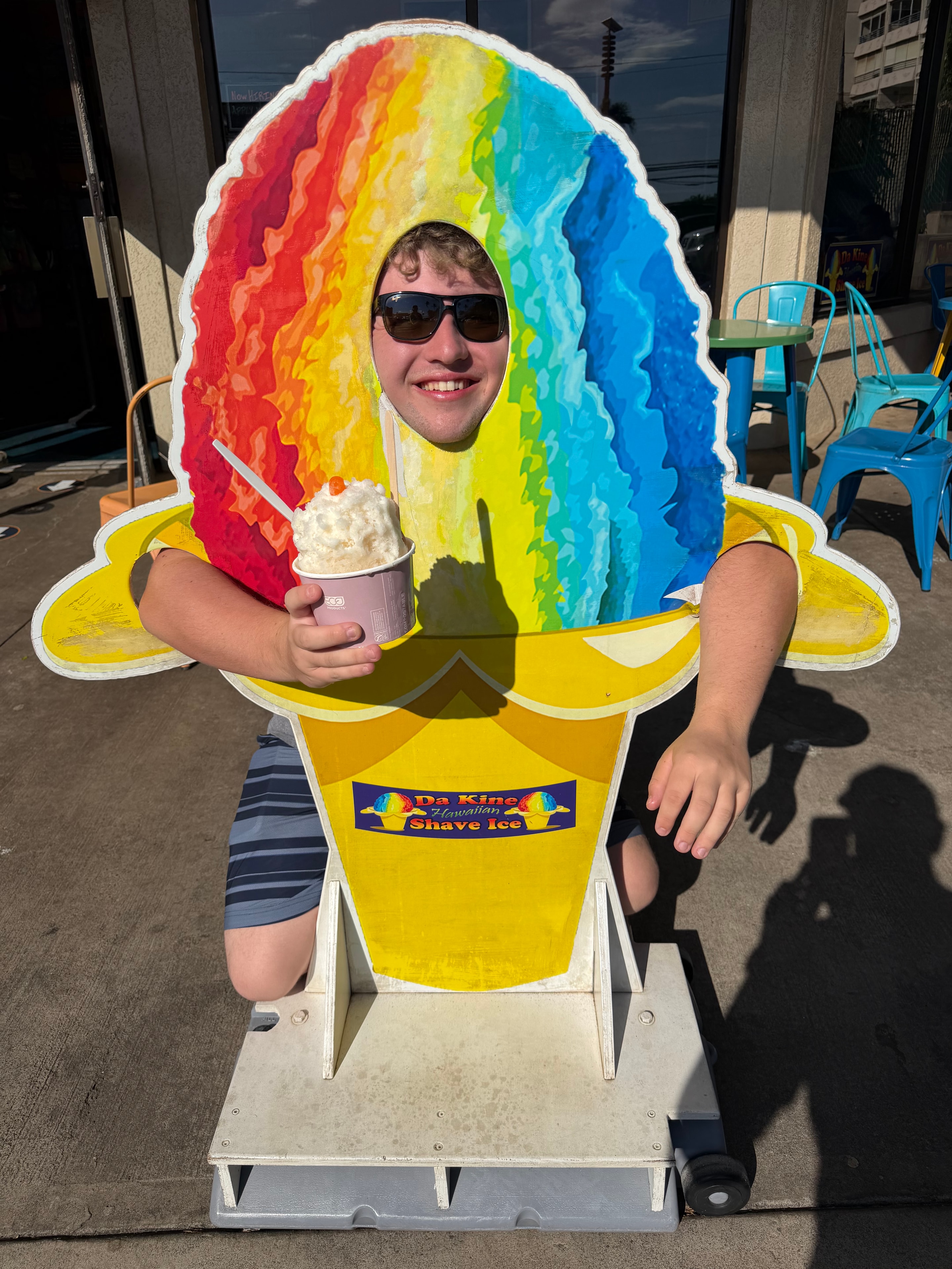 Person posing through a rainbow shave ice photo cutout at a Shaka Shak event